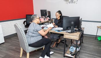 two women sitting at a desk in front of a computer